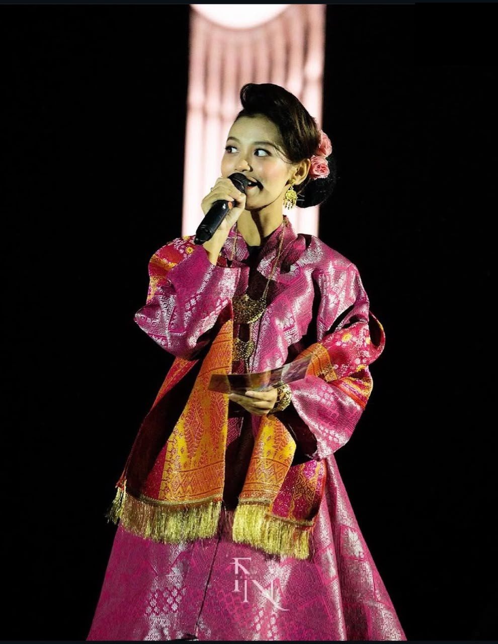 Bella hosting on stage in traditional pink and gold attire